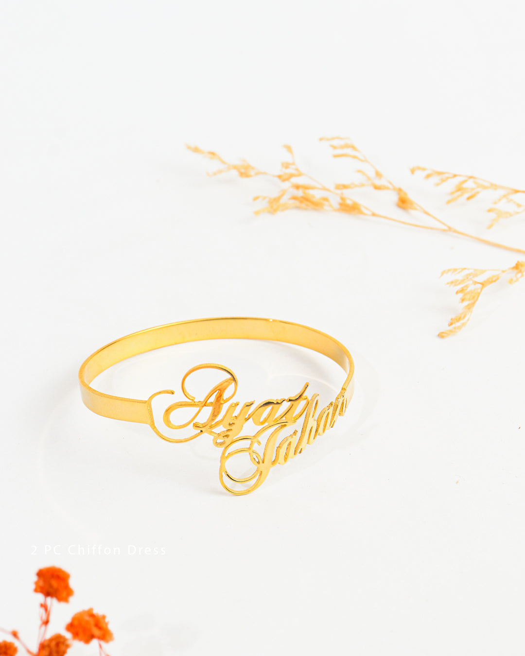 Gold bracelet with cursive text on a white background with orange flowers
